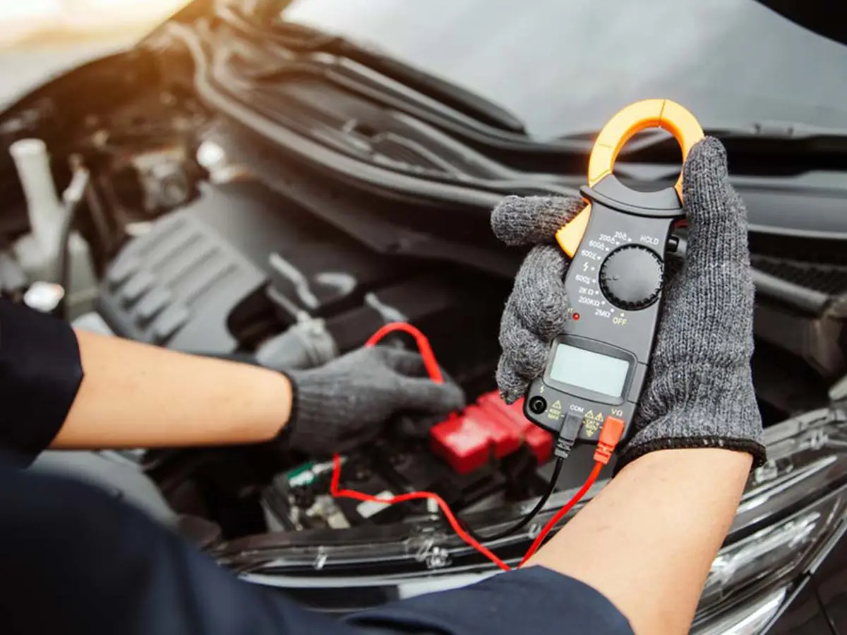 Mecanic auto verificând tensiunea bateriei cu un multimetru digital